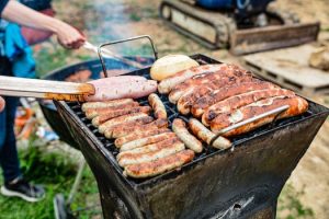 Grilling an assortment of sausages and bread at an outdoor barbecue on a sunny day.